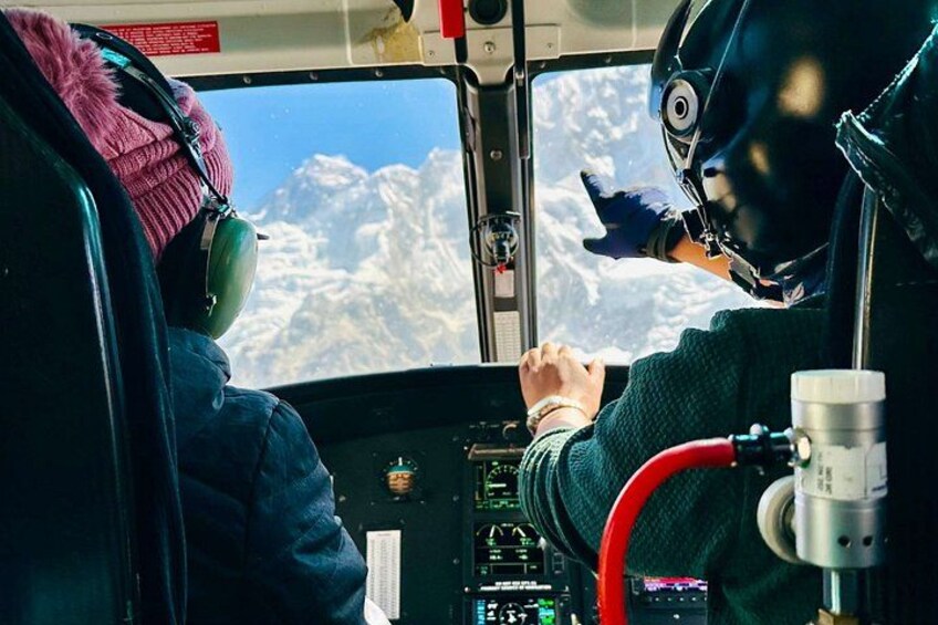 Cabina di elicottero con pilota e passeggero, un pannello di controllo e vista di montagne innevate dalla finestra. 4