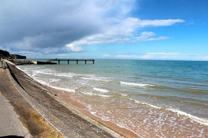A beach with waves, a pier, and a cloudy sky. 1