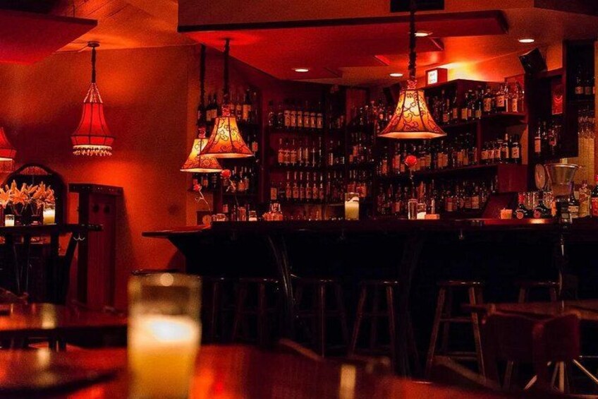Un bar dall'illuminazione soffusa con luci rosse ambientali, lampade a sospensione e un bancone con sgabelli. 5