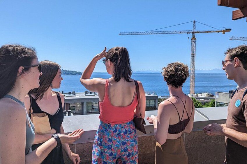 Un gruppo di persone in piedi su un tetto con vista su un'area lacustre, con una gru edile sullo sfondo. 2