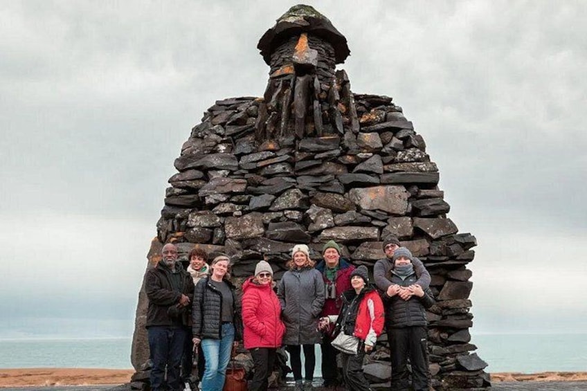 A group of people standing in front of a stone structure with a view of the sea in the background. 5