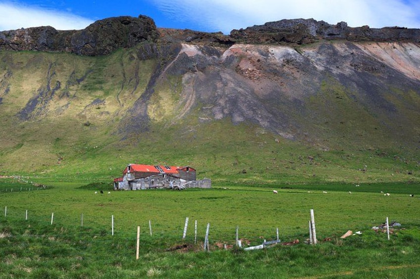A rural landscape with a red-roofed house, green fields, and a rocky mountain in the background. 3