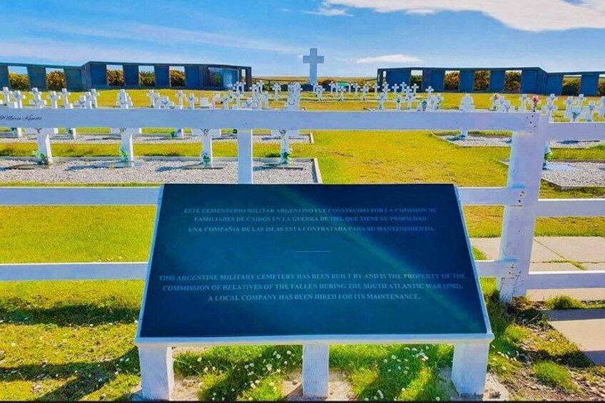 A cemetery with white crosses and a sign in the foreground. 1