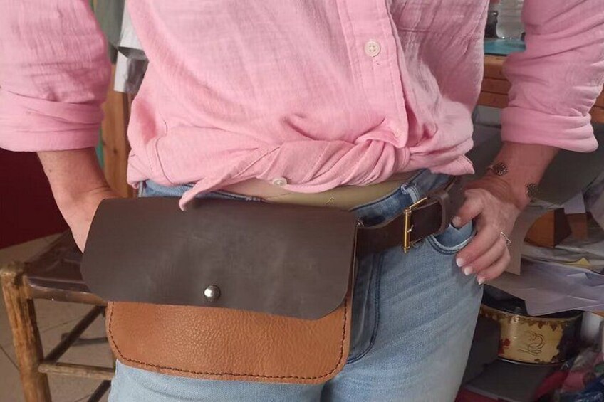 Una persona con camisa rosa, jeans azules, cinturón de cuero marrón y bolso de cuero marrón con hebilla metálica. 4