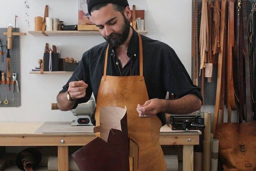 Una persona trabajando con delantal de cuero en un taller, con herramientas y materiales de cuero. 1
