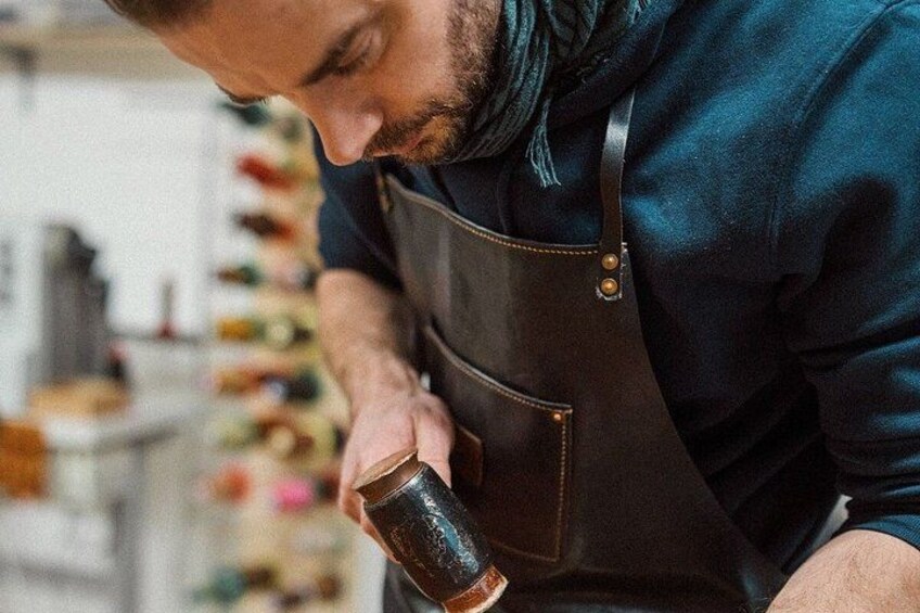 Una persona con delantal oscuro y camisa azul, sosteniendo un objeto de color oscuro. 5