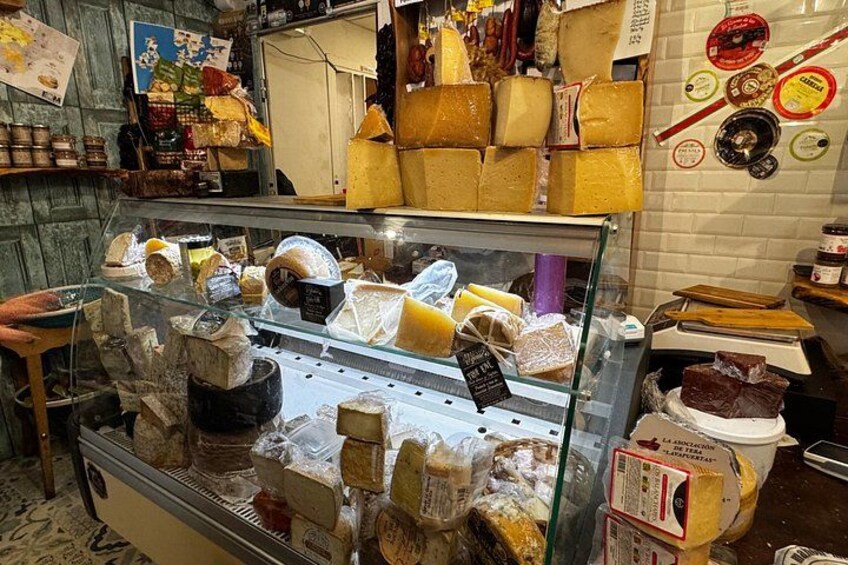 A cheese shop with a glass display case filled with various cheeses and cheese wheels. 5