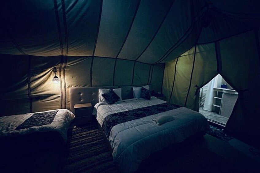 A tent with two beds, a nightstand, and a small table. 3