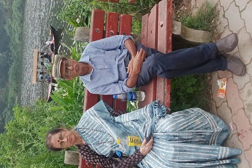 Two people sitting on a bench by a river, with boats in the background. 3