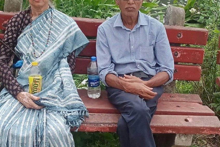Two people sitting on a red bench in a park with greenery in the background. 4