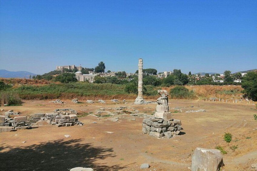 Ancient ruins with stone columns and scattered stones, a clear sky, and distant buildings. 2