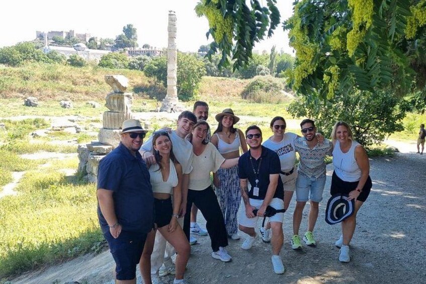 A group of people posing in a historical site with ruins and a tall column in the background. 1