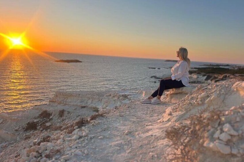 Una persona sentada en una costa rocosa al atardecer. 1
