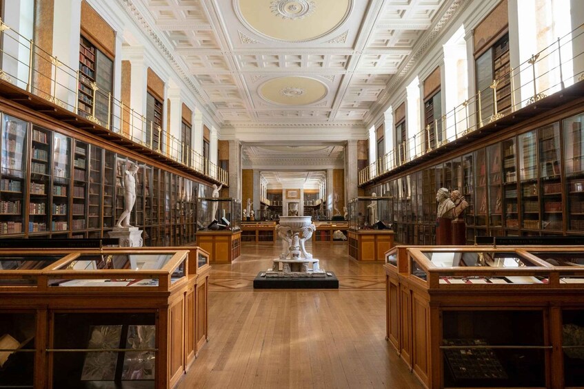 A grand library with wooden bookshelves, marble statues, and ornate ceiling details. 3