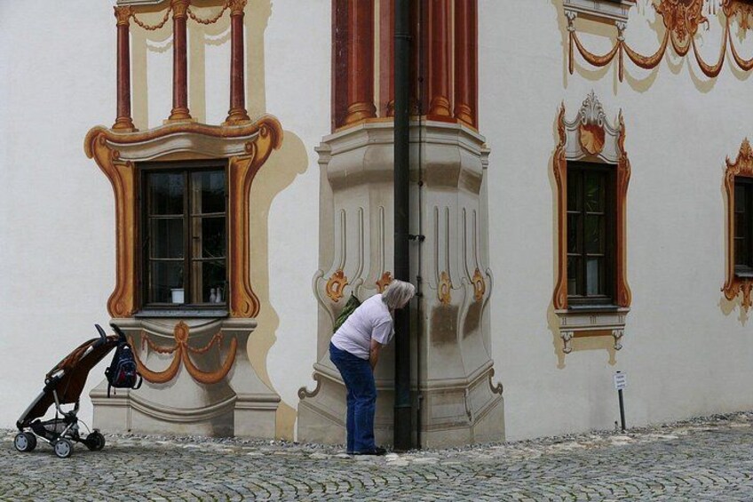 Una persona de pie junto a un edificio con marcos de ventanas ornamentales y un cochecito cerca. 3