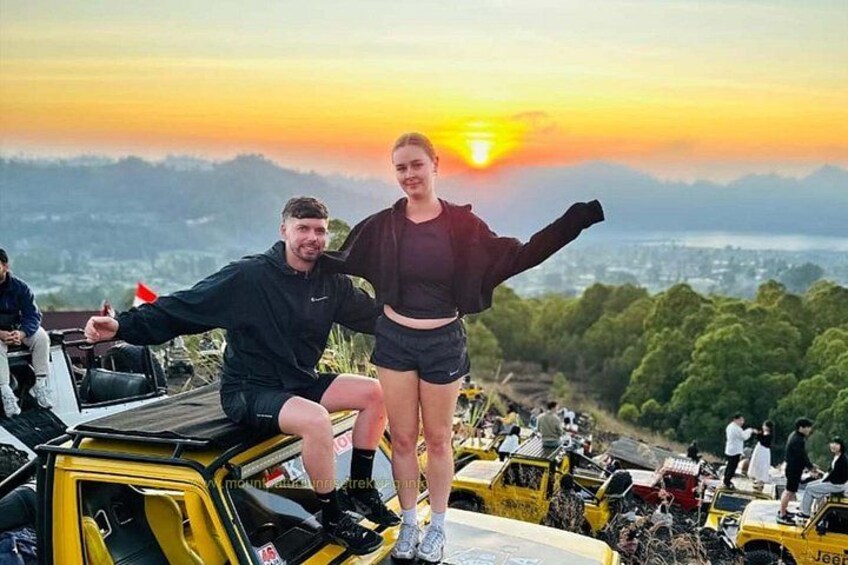 Dos personas en un vehículo con el atardecer al fondo. 1
