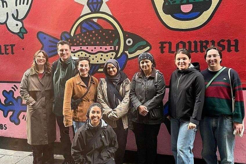 Eine Gruppe von Personen steht vor einer Wand, auf der ein Fisch und das Wort 'FLOURISH' abgebildet sind. 4