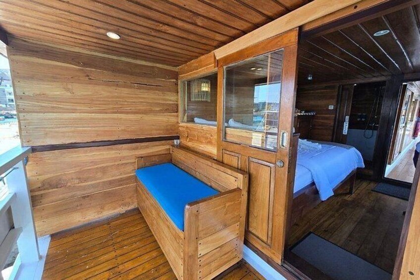 Eine Holzhütte mit einer blauen gepolsterten Bank, einem Bett mit weißer Bettdecke und einer Holztür. 2