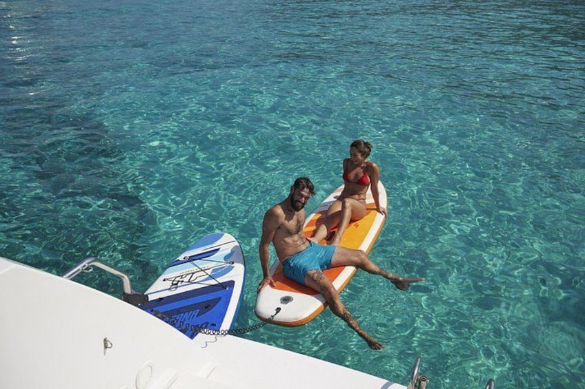 A man and a woman sitting on a surfboard in clear blue water. 5