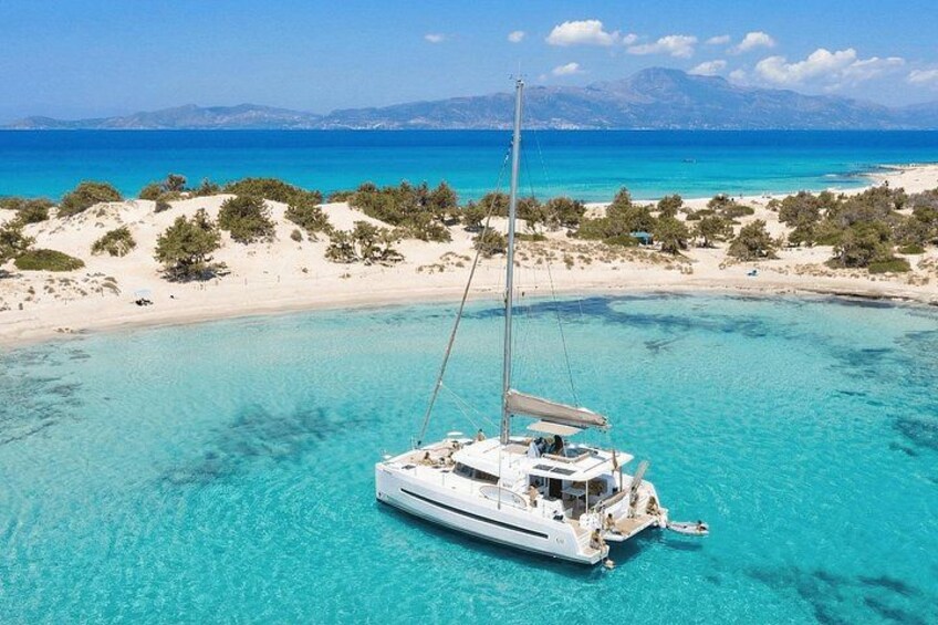 A sailboat on turquoise waters with a beach and trees in the background. 1
