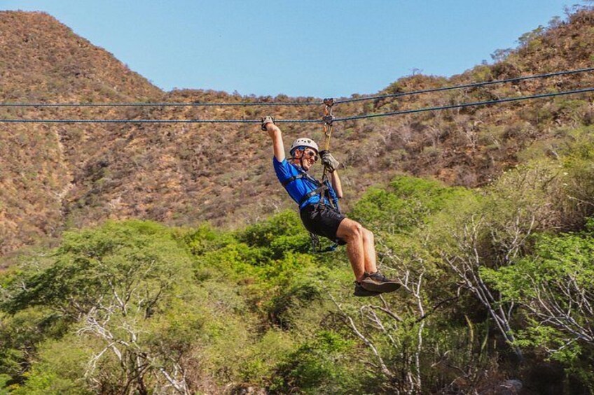 A person zip-lining through a forested area with a clear sky and hills in the background. 4