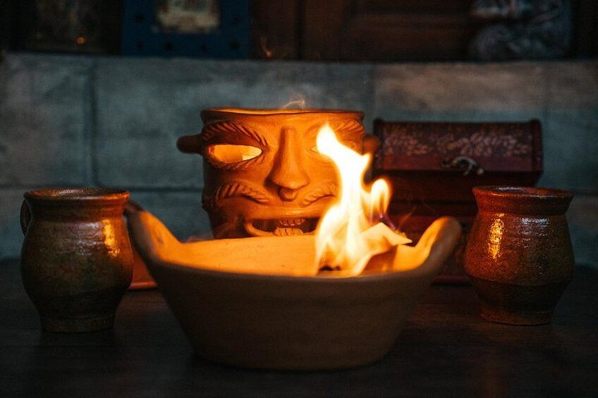 Una olla de arcilla con rostro, un cuenco con llamas y dos pequeñas macetas sobre una mesa. 1