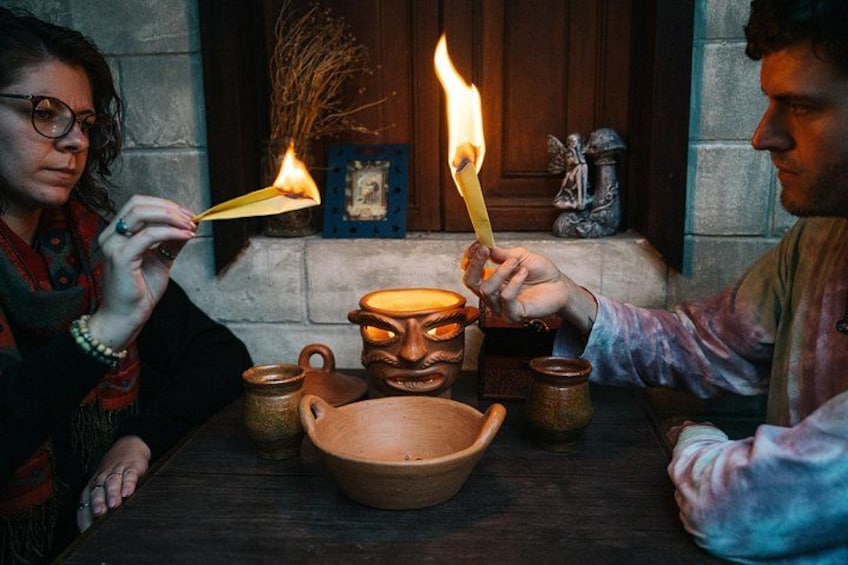 Una persona sosteniendo un fósforo encendido, una olla de barro y un cuenco sobre una mesa. 4