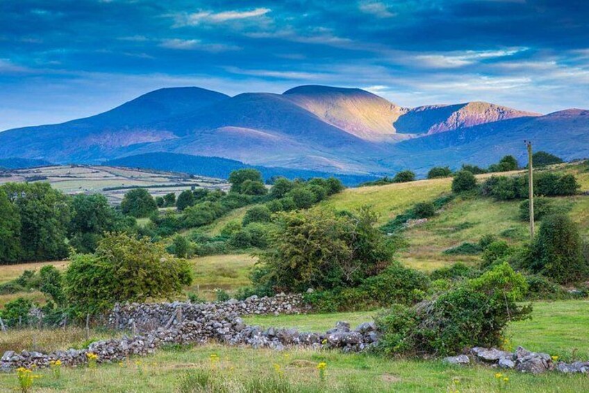 A mountainous landscape with a stone wall, green fields, and a clear sky. 4