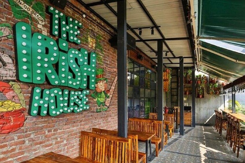 A brick wall with a green sign reading 'The Irish House,' wooden benches, and a covered outdoor seating area. 5