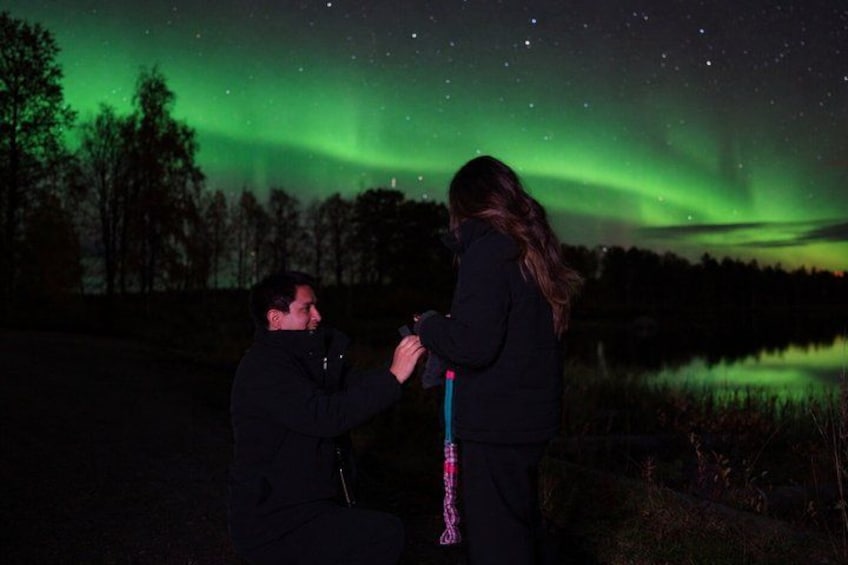 A person kneeling and proposing to another person under a night sky with green aurora. 2