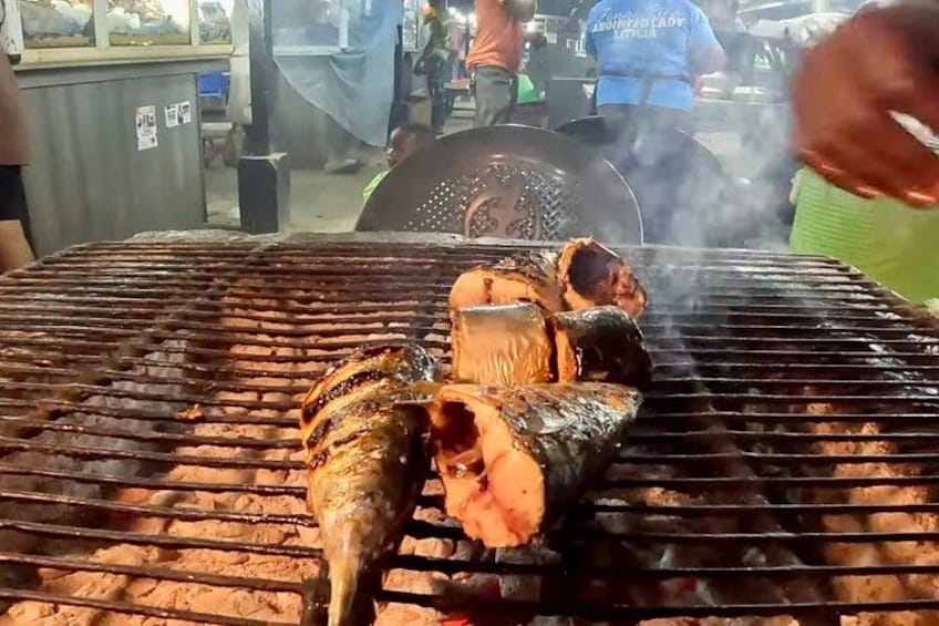 Ge grillter Fisch auf einem Grill, eine Person würzt ihn. 2