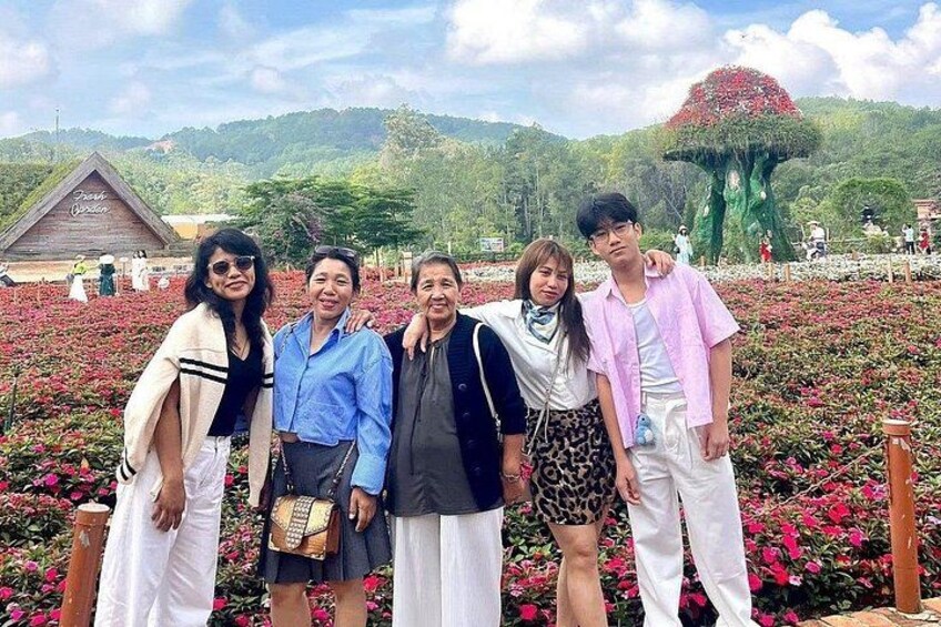 A group of people standing in a flower field with a large tree structure in the background. 4