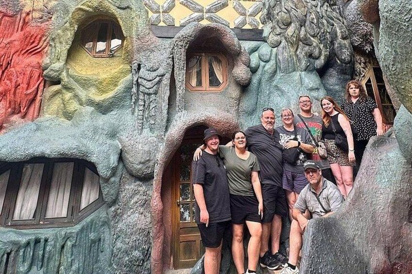 A group of people posing in front of a whimsical, textured building with a face-like facade. 5