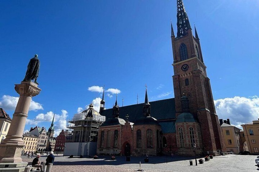 Una iglesia histórica con una aguja alta, una estatua en primer plano y un cielo azul despejado. 5