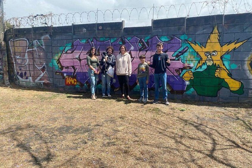 Un groupe de personnes se tient devant un mur couvert de graffitis, sur lequel on peut voir un personnage en forme d’étoile. 5