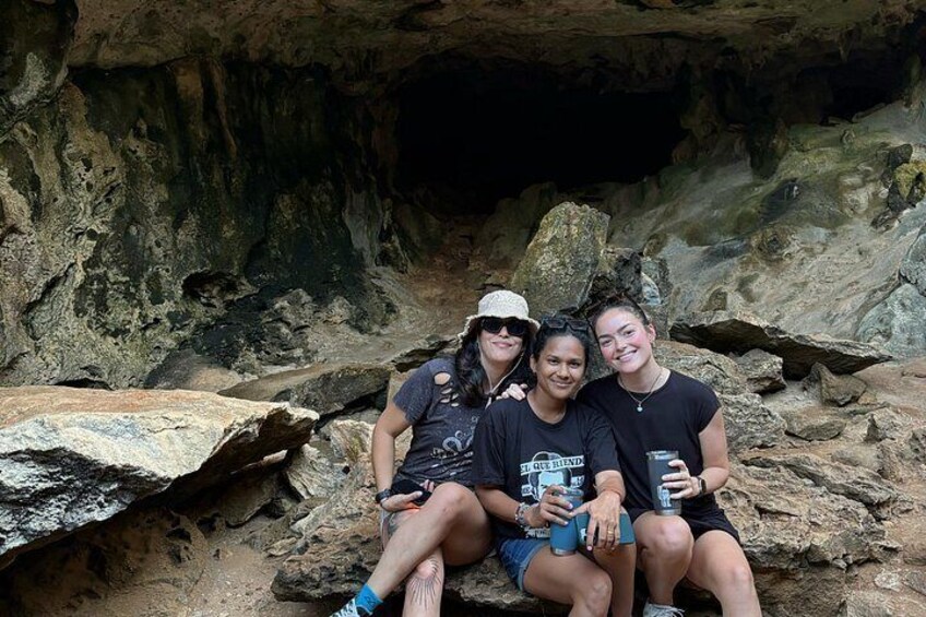 Trois personnes sont assises sur des rochers dans une grotte, avec une paroi rocheuse de la grotte en arrière-plan. 3