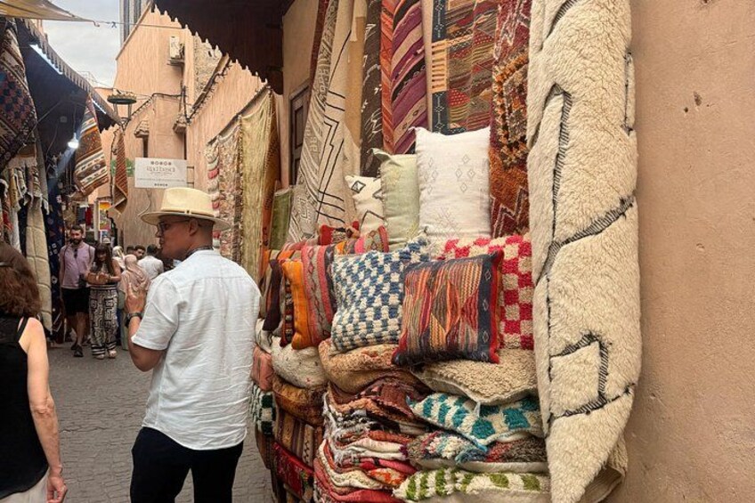 A narrow street with a variety of textiles displayed on a wall, including blankets and pillows. 2