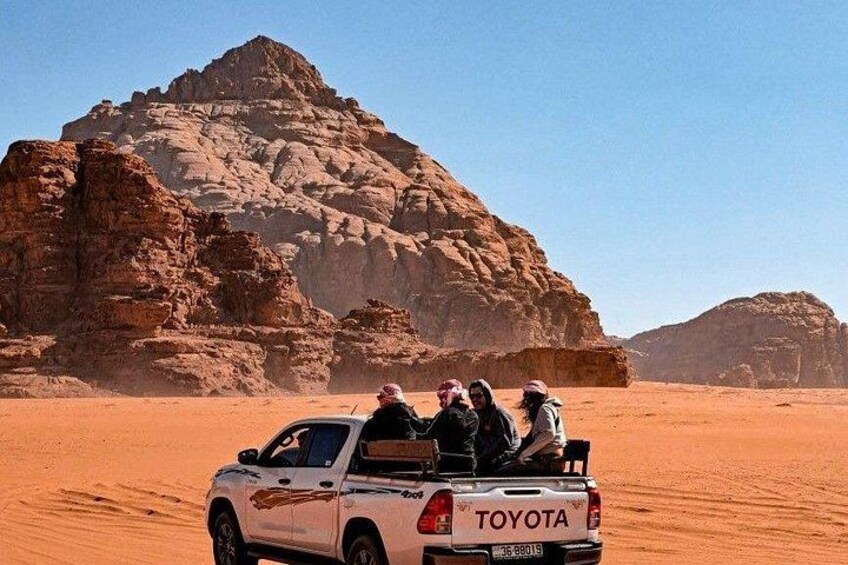 Una camioneta Toyota blanca con cuatro pasajeros en un paisaje desértico con grandes formaciones rocosas. 3