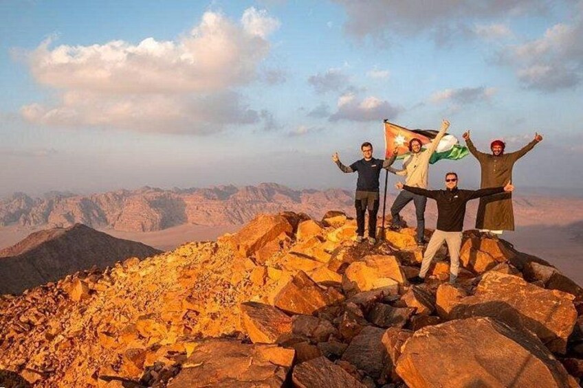 Un grupo de personas en la cima de una montaña rocosa con una bandera, bajo un cielo despejado. 1