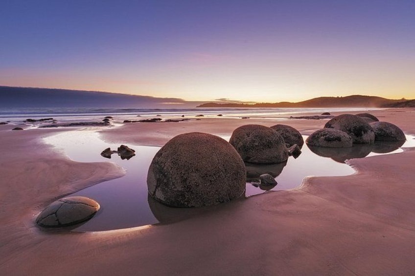A beach with large rocks and calm water at sunset. 3