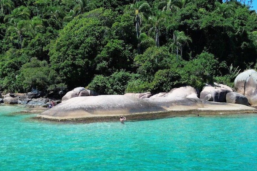 A turquoise sea with large rocks and a forested island in the background. 1
