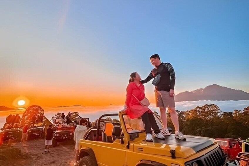 Atardecer con una pareja en un vehículo, una montaña al fondo y otros vehículos estacionados. 2