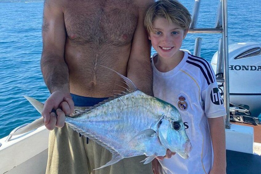 A person holding a fish, a boat, and a water body. 4