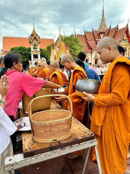 Monks in orange robes serving food to a woman in a pink shawl at a temple with ornate architecture. 1