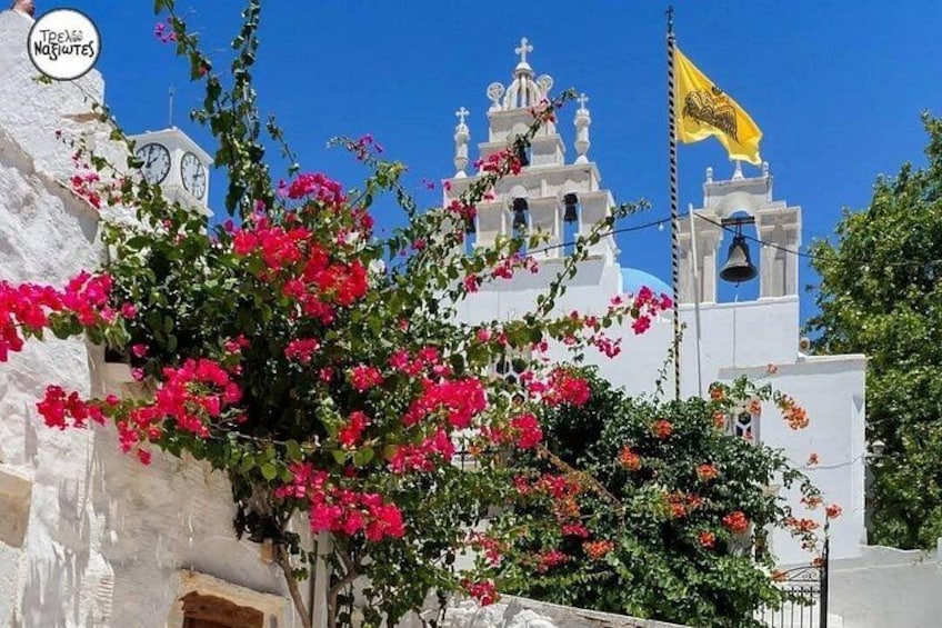 En vit kyrka med röda blommor, en gul flagga och en blå himmel. 3