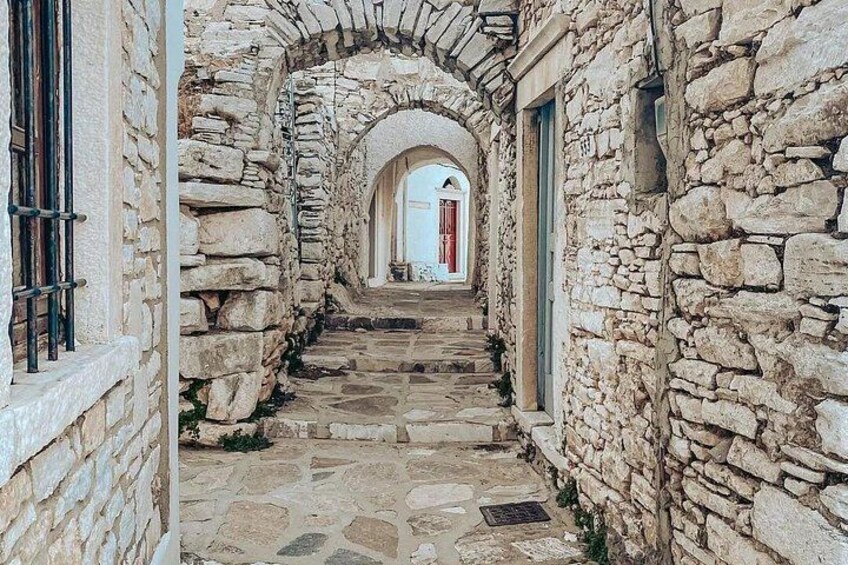 A stone pathway leading through an arched stone corridor with a building entrance in the distance. 3
