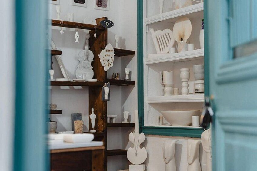 A room with shelves displaying white ceramic items, a wooden structure with hanging items, and a teal door. 3