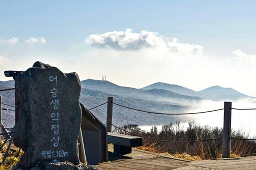 Un monumento in pietra con testo coreano, una recinzione in legno e un paesaggio montuoso sullo sfondo. 1