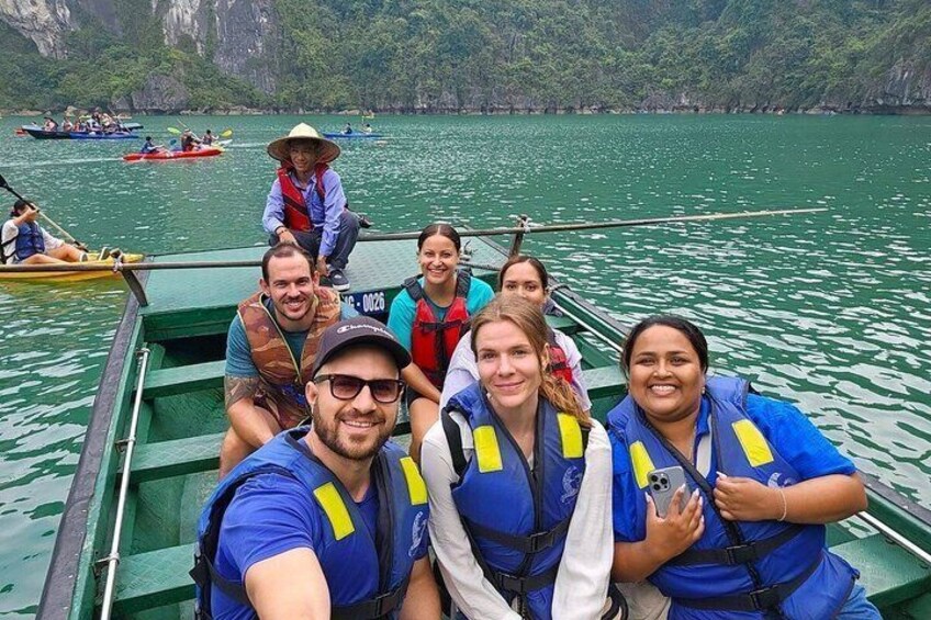 A group of people on a green boat with life jackets, surrounded by calm water and distant rocky cliffs. 4