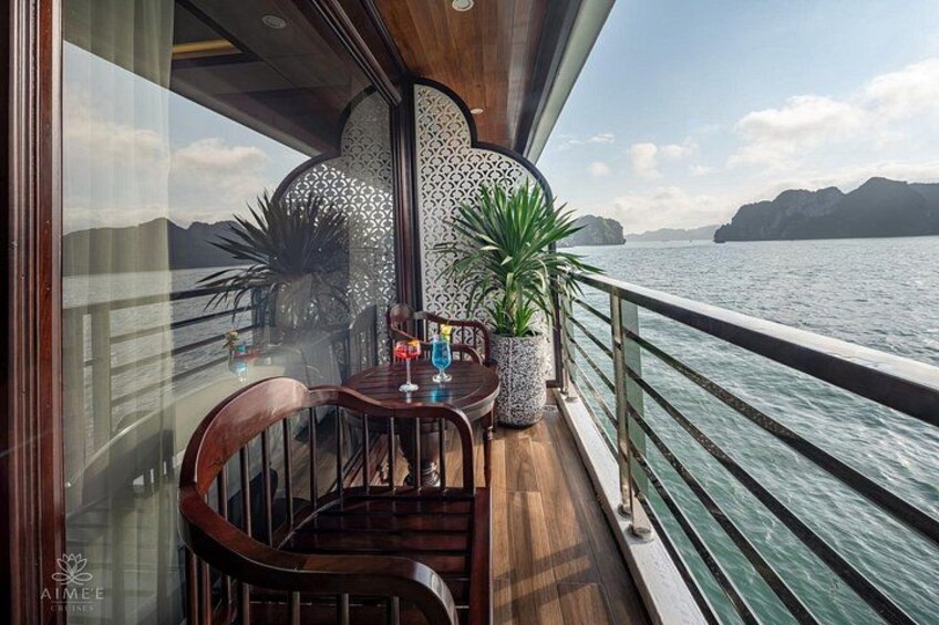 A deck with a table, chairs, potted plants, and a view of the water and distant land. 2